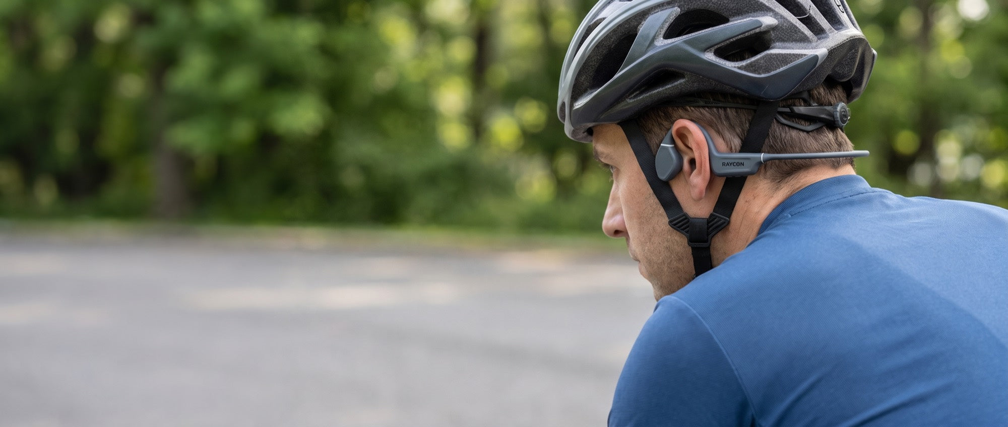 A cyclist on a tree-lined road wearing the Bone Conduction Headphones under a helmet