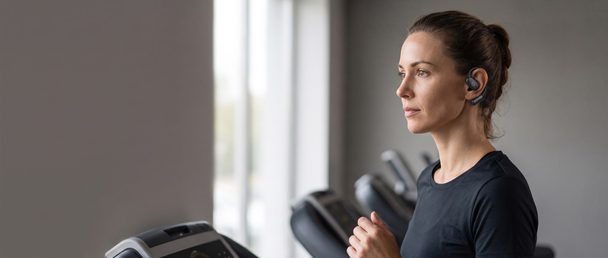 A runner on a treadmill in a quiet gym wearing the Essential Open Earbuds, ear canal open