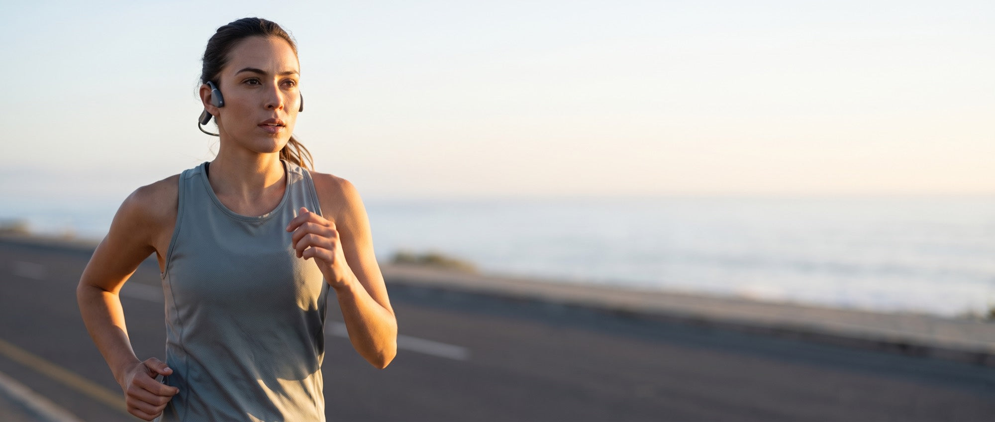 A runner on a coastal road at sunrise wearing the Bone Conduction Headphones, ears open